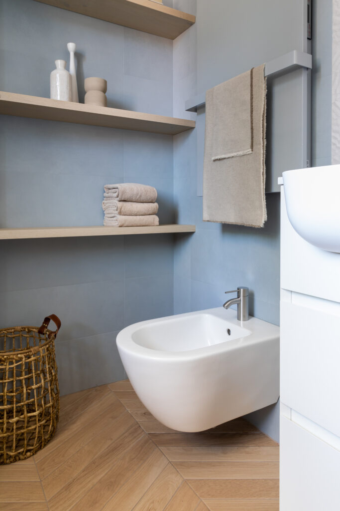 angolo bagno moderno con bidet sospeso, mensole legno, radiatore d'arredo in tinta con piastrelle azzurro carta da zucchero 